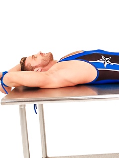 Hot wrestler tied to a table in his spandex outfit struggles against the bondage